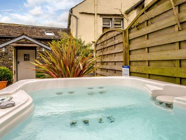 An outdoor hot tub with water next to a wooden fence and a stone building at Shepherds Cottage in Hawkshead