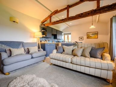 A living room with two sofas, a floor lamp, exposed wooden beams, and a kitchen area at Shepherds Cottage in Hawkshead