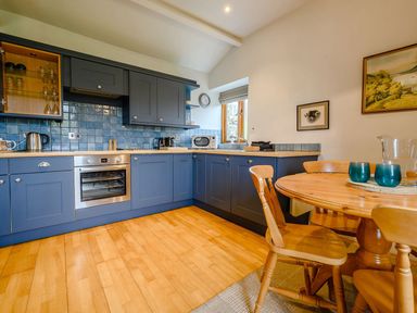 A kitchen with blue cabinets and wooden dining table at Shepherds Cottage in Hawkshead