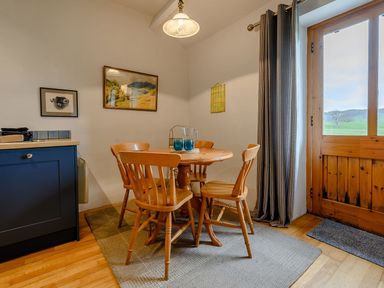 A dining area with a round wooden table and four wooden chairs near a window and cabinet at Shepherds Cottage in Hawkshead