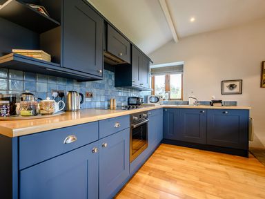 A kitchen with blue cabinets wooden countertops a window and various kitchen appliances at Shepherds Cottage in Hawkshead