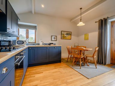 A kitchen with blue cabinets wooden countertops a round wooden dining table with chairs and a window at Shepherds Cottage in Hawkshead
