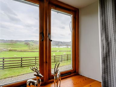 A wooden window with two deer figurines on the sill overlooking green fields and sheep at Shepherds Cottage in Hawkshead