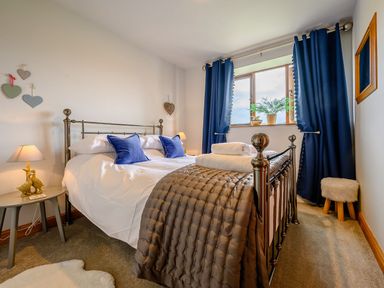 A bedroom with a double bed with blue pillows and folded towels with blue curtains on the window at Shepherds Cottage in Hawkshead