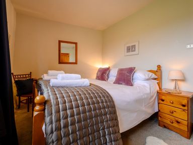 A bedroom with a wooden bed with pillows blankets and towels with a bedside table lamp and chair at Shepherds Cottage in Hawkshead