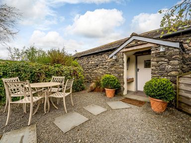 An outdoor seating area with a table and four chairs outside a stone cottage with potted plants at Shepherds Cottage in Hawkshead