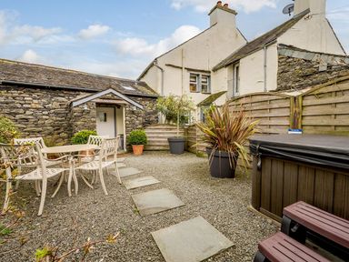 An outdoor patio area with a table and chairs surrounded by stone buildings and a wooden fence at Shepherds Cottage in Hawkshead