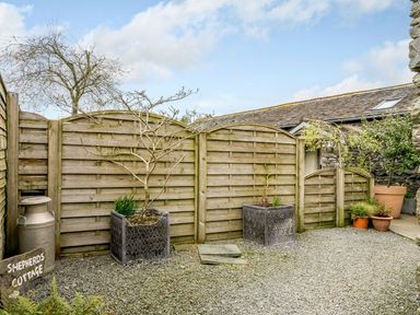 A gravel yard with wooden fence potted plants and a metal milk can at Shepherds Cottage in Hawkshead