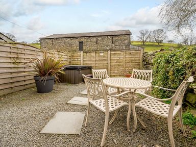 An outdoor patio with a metal table and chairs a large potted plant a hot tub and wooden fencing at Shepherds Cottage in Hawkshead