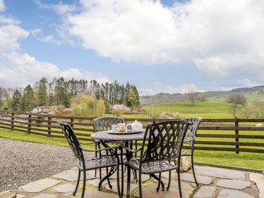 An outdoor patio with a metal table and four chairs overlooking green fields and trees at Shepherds Cottage in Hawkshead