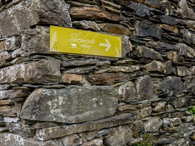 A stone wall with a yellow sign pointing to Shepherds Cottage in Hawkshead