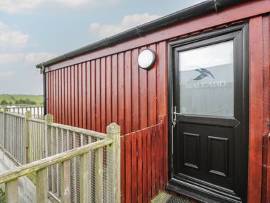 An exterior red wooden building with a black door labeled Mallard and a wooden railing surrounding a walkway at Mallard Lodge in Moscow near Galston