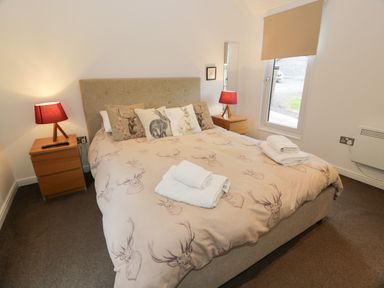 A bedroom with a bed with animal print duvet and pillows two wooden bedside tables with red lamps at Mallard Lodge in Moscow near Galston