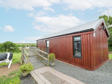 A wooden building with a deck and grassy area at Mallard Lodge in Moscow near Galston