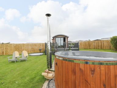 A garden with a wooden hot tub chairs and a small wooden house behind a fence at Greenacres Carriage in Maybole