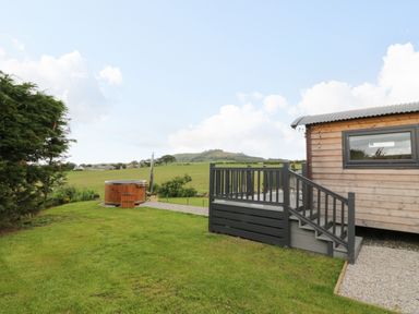 A wooden cabin with a small porch and steps next to a grassy yard and a round wooden hot tub at Greenacres Carriage in Maybole