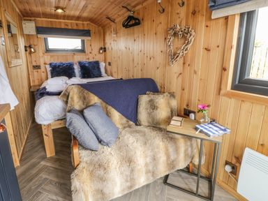 A small bedroom with a bed towels a fur-covered chair and a side table with a flower at Greenacres Carriage in Maybole