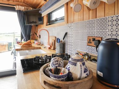 A kitchen counter with a stove sink teapot and cups with blue and white tiles on the wall at Greenacres Carriage in Maybole