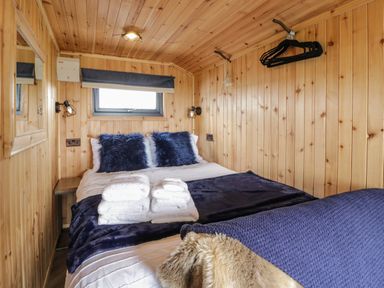 A bedroom with wooden walls a bed with navy blue pillows folded towels on the bed and hangers on the wall at Greenacres Carriage in Maybole