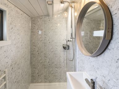 A bathroom with a shower, round mirror, sink, and marble patterned walls at Greenacres Carriage in Maybole