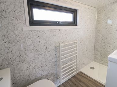 A bathroom with a window a white towel rack a shower area and a wooden floor at Greenacres Carriage in Maybole