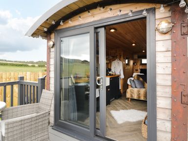 A small wooden cabin interior with sliding glass door and outdoor wicker chair at Greenacres Carriage in Maybole