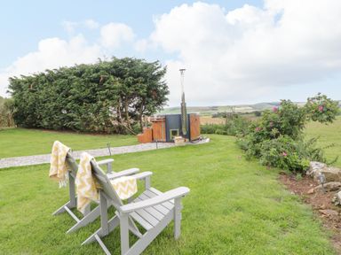 Two wooden chairs with yellow blankets on a lawn near a hot tub and bushes at Greenacres Carriage in Maybole