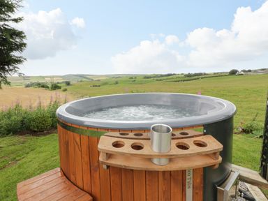 An outdoor wooden hot tub with bubbling water and a cup holder overlooking green fields at Greenacres Carriage in Maybole