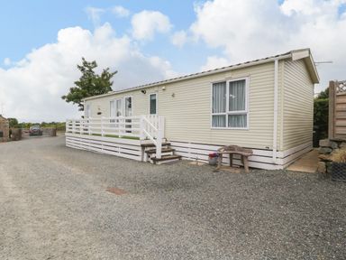 A beige mobile home with white railings and steps on a gravel driveway at Gwel Eryri in Penmynydd near Llanfairpwllgwyngyll