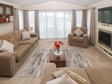 A living room with brown sofas a coffee table with flowers a wall mounted television and large windows at Gwel Eryri in Penmynydd near Llanfairpwllgwyngyll