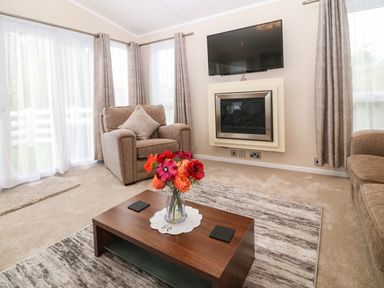 A living room with armchairs a coffee table with flowers a rug and a wall-mounted television above a fireplace at Gwel Eryri in Penmynydd near Llanfairpwllgwyngyll