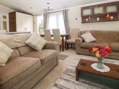 A living room with two beige sofas a wooden coffee table with a vase of flowers four dining chairs and a wall cabinet at Gwel Eryri in Penmynydd near Llanfairpwllgwyngyll