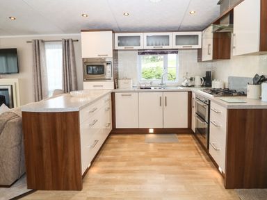 A kitchen with white cabinets wooden accents a microwave stove and a sink at Gwel Eryri in Penmynydd near Llanfairpwllgwyngyll