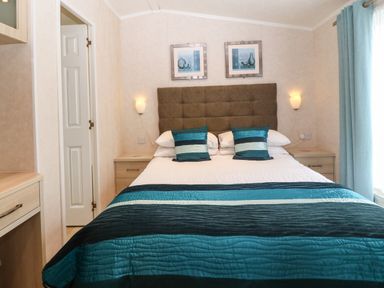 A bedroom with a bed with blue and white striped pillows and bedspread two wall lamps and two pictures above the headboard at Gwel Eryri in Penmynydd near Llanfairpwllgwyngyll