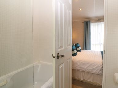 A bathroom with a bathtub and a partially open door leading to a bedroom with a bed and blue curtains at Gwel Eryri in Penmynydd near Llanfairpwllgwyngyll