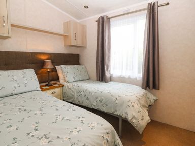 A bedroom with two beds a bedside table with a lamp and a window with curtains at Gwel Eryri in Penmynydd near Llanfairpwllgwyngyll