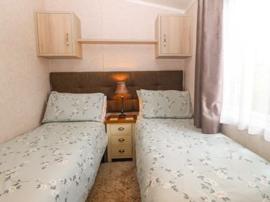 A bedroom with two single beds a bedside table lamp and wall cabinets at Gwel Eryri in Penmynydd near Llanfairpwllgwyngyll