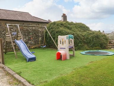 A backyard with children's play equipment including a slide swing set climbing frame and trampoline at Gwel Eryri in Penmynydd near Llanfairpwllgwyngyll