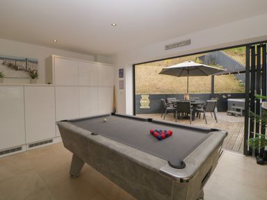 A room with a pool table and white cabinets opening to an outdoor patio with a table umbrella and chairs at 12 Beachdown in Challaborough