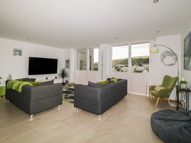 A living room with two dark sofas a green armchair a bean bag and a wall mounted TV at 12 Beachdown in Challaborough