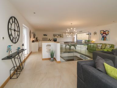 An open living area with couches a large wall clock a pool table and a kitchen at 12 Beachdown in Challaborough