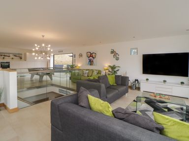 A living room with gray and green sofas a glass coffee table and a large wall-mounted TV at 12 Beachdown in Challaborough