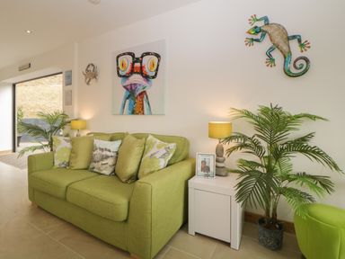 A green sofa with cushions and a side table with lamp and photo frame in a living room at 12 Beachdown in Challaborough