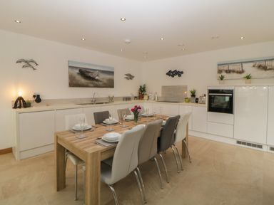 A kitchen with a wooden dining table set for eight and white cabinets at 12 Beachdown in Challaborough