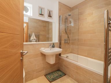 A bathroom with a sink a bathtub shower and a beach themed mat at 12 Beachdown in Challaborough