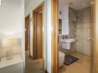 A hallway with wooden doors leading to a bathroom with a sink toilet and shower at 12 Beachdown in Challaborough
