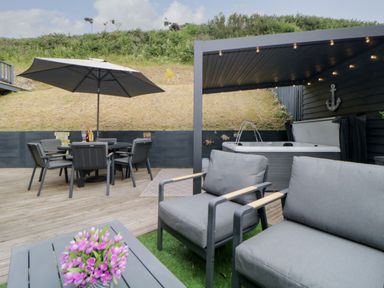 An outdoor patio with a dining table and umbrella seating area with a hot tub under a covered structure at 12 Beachdown in Challaborough