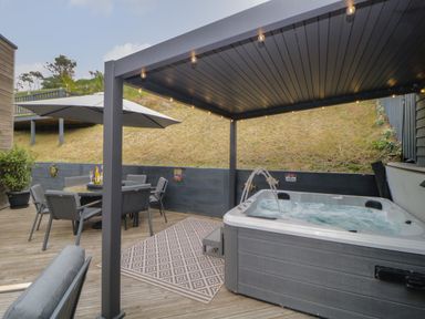 An outdoor deck with a covered hot tub a dining table with chairs and an umbrella at 12 Beachdown in Challaborough