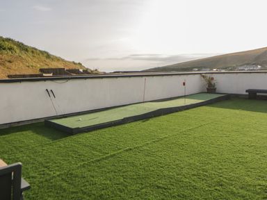 An outdoor putting green with two golf clubs and two flags on a grassy rooftop at 12 Beachdown in Challaborough