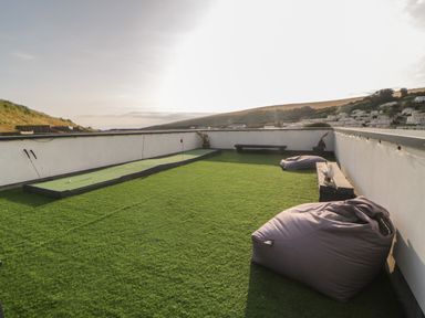 A rooftop patio with artificial grass a putting green two gray bean bag chairs and a wooden bench at 12 Beachdown in Challaborough